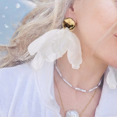 Close-up of a person wearing gold earrings and a necklace with a pendant, outdoors.