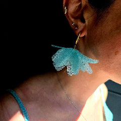 Close-up of a person wearing light blue floral earrings.